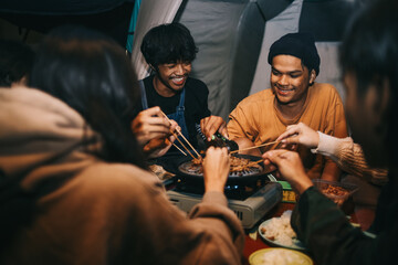 Group of Asian friends grilling meat at dinner time while camping in forest