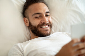 Guy using smartphone browsing internet lying in bed