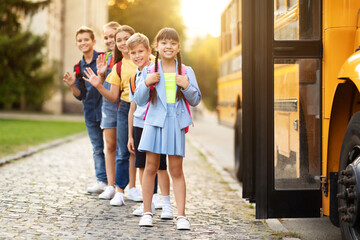 Children with backpacks standing in line beside school bus