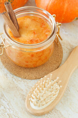 Homemade pumpkin face mask (scrub) in a glass jar and wooden hairbrush. Natural autumn beauty treatment and spa recipe.