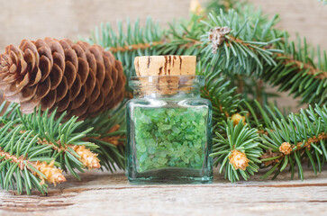 Small bottle with green aroma bath salts (foot soak) with coniferous tree extract. Christmas aromatherapy. Winter spa and herbal medicine concept. Old wooden background.