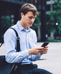 Young businessman in wireless headphones chatting on phone outdoors