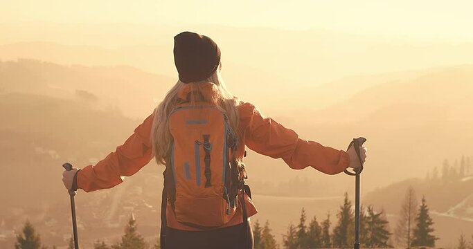 Woman hiker, hiking backpacker traveler camper walking on the top of mountain in sunny day under sun light. Beautiful mountain landscape view, nordic walking