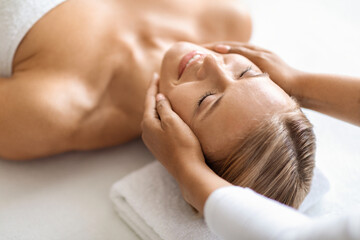 Attractive middle aged woman having revitalizing face lifting massage at spa salon
