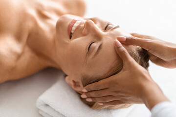 Relaxed middle aged woman enjoying acupressure head massage at luxury spa salon