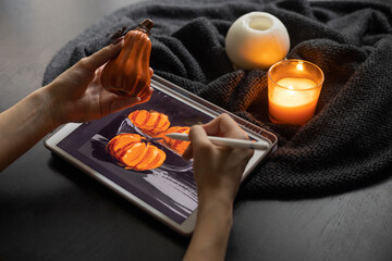 Girl's hands draw still life picture with pumpkins on electronic tablet near burning candle. The concept of inspiration, creativity, modern art. Halloween, Thanksgiving day. Autumn, fall