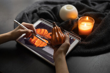 Girl's hands draw still life picture with pumpkins on electronic tablet near burning candle. The concept of inspiration, creativity, modern art. Halloween, Thanksgiving day. Autumn, fall