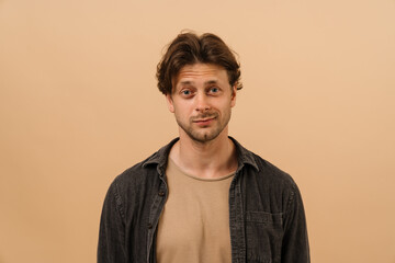 Young man smiling at camera while standing isolated over beige wall
