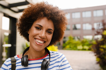 Fototapeta premium Portrait of happy female student smiling at camera while standing in campus