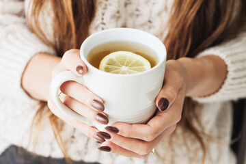 Hot tea in a mug. Woman holding mug of lemon tea. Cold winter relax background. Woolen sweater warm...