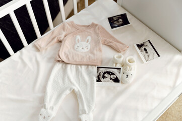 An ultrasound scan and baby clothes are lying in a child's bed. crib for a newborn. waiting for the...
