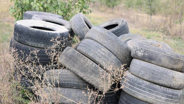 stack of used and used car tires in orchard with trees. rubber tyre stuck outside 4k
