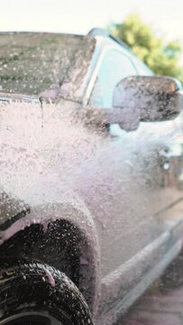 Male driver wringing out a washcloth with water and pink nano foam while washing his car at a self-service car wash