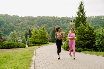 Two smiling women running together in park