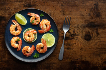 Shrimps with lime, overhead flat lay shot, with copy space. Cooked shrimp on a blue plate, shot from the top on a rustic wooden background