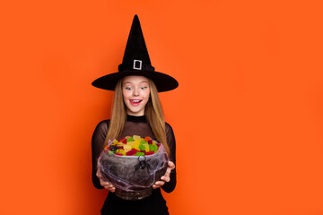 Photo portrait of pretty blonde teenager girl hold candies lick lips dressed black halloween outfit...