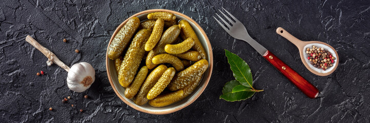 Pickled cucumbers with salt, pepper, garlic, and bay leaf panorama. Fermented food. Homemade canned gherkins. Overhead flat lay shot on a black slate background, panoramic banner