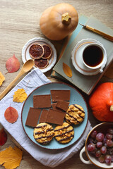 Cup of tea or coffee, plate with cookies and chocolate, dried oranges, bowl of grapes, vintage books, pumpkins and autumn leaves on the table. Autumnal hygge. Top view.