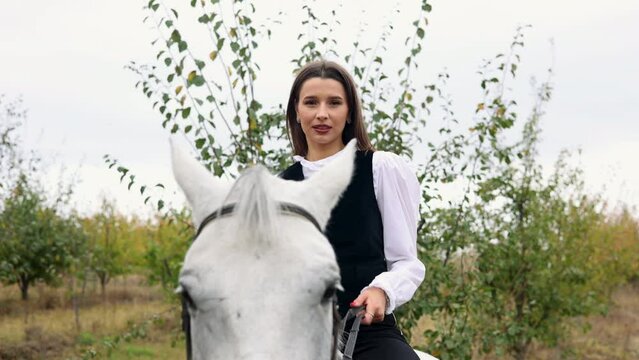 portrait of beautiful woman riding horse in orchard,touches horse muzzle, with forehead glued from animal head.girl calms horse with hand.female and anima in embrace,hugging neck,closed eyes.