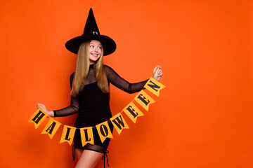 Photo of attractive blonde teen woman look empty space hold garland dressed black halloween clothes isolated on orange color background