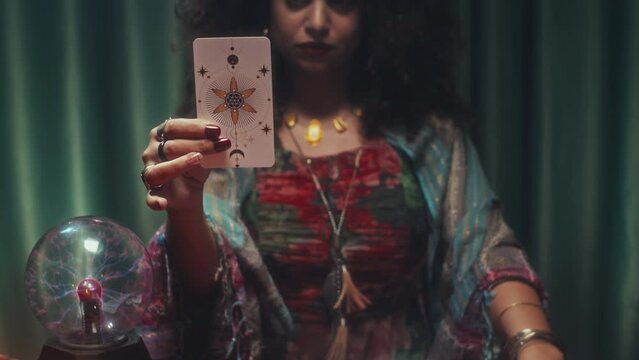 Tilt up shot of woman taking one card from tarot layout and showing to camera during clairvoyance session