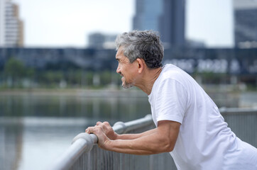 older adult male stretching arms walkway steel railing by the pond in the city,healthy senior man...
