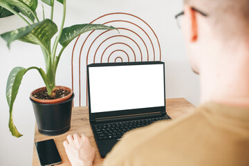  Blank white screen place for text or template. Man at home uses laptop mockup. Modern technology in everyday life.  European young man using a laptop for remote work from home.