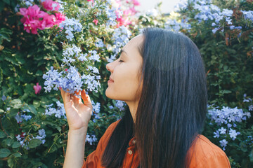 A young beautiful smiling woman stands near a flowering bush in the garden and enjoys the fragrance of flowers. Spring concept