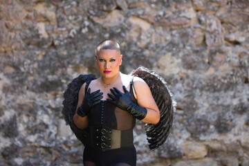 Young non-binary Latin person, wearing black make-up and black dress, with black angel wings, covering his chest with his hands. Concept of diversity, homosexuality and human rights.