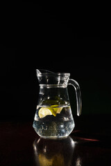 huge thirst quenching and fresh jug of clear water with small slices of lemon on black backdrop