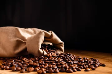 Fotobehang Fresh roasted coffee beans falling out the sack on the wooden surface. Brown coffee beans scattered from bag on the table. © Vladimir