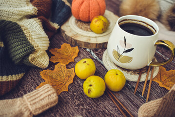 Cup of coffee with autumn leaves, quinces and knitted scarf on wooden background