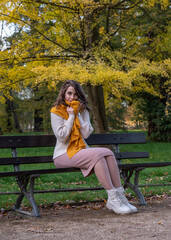 attractive young smiling woman sitting on a bench in an autumn park, wrapped in a yellow shawl, happy mood, fashion style trend.