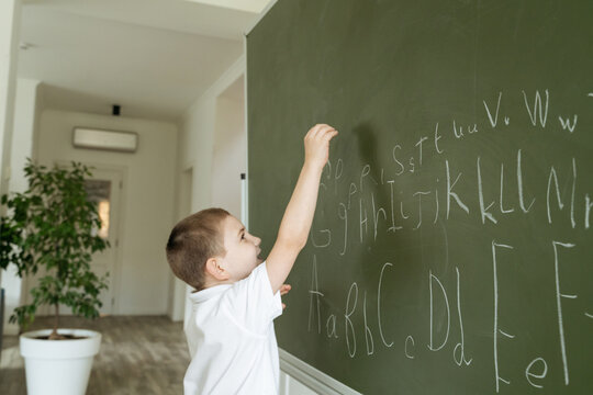 Boy writing abc letters on the green chalkboard - Powered by Adobe