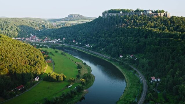 Aerial drone flight over idyllic landscape of the Saxon Switzerland with forests, fields and the river Elbe with the K&ouml;nigstein Fortress above it.