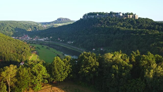 Aerial drone flight over idyllic landscape of the Saxon Switzerland with forests, fields and the river Elbe with the K&ouml;nigstein Fortress above it.