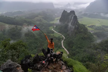 Deurstickers Tourist holding Lao flag on the Nam Xay Viewpoint, During the rainy season in Vang Vieng, Laos. © tonjung