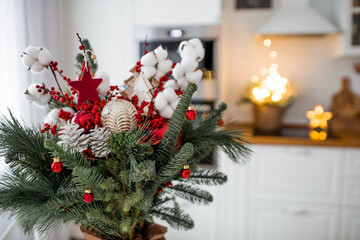 A spruce bouquet with red berries, toys, cotton on a white kitchen table. Christmas decorations in the interior. The concept of preparation for the New Year's holiday 2024.
