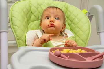 Baby wearing knitted sweater sitting in high chair and feels hungry, holding spoon and eating puree or porridge, enjoying apples and water in yellow bottle, posing isolated on white background.