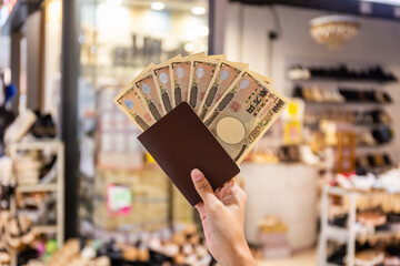Japanese 10,000 yen banknote in hand and tourist passport used to buy and sell goods, traditional demon mask background. Select focus