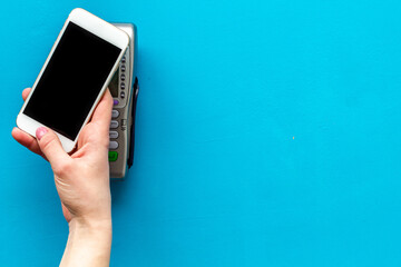 Female hand with mobile phone near POS payment terminal. Payment by mobile pay