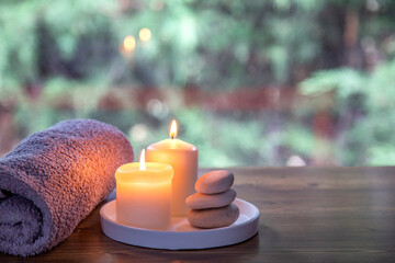 two candles towel and white stones on wooden table agains green nature background. Spa still life...