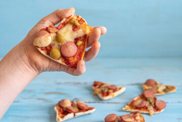 Mini pizza in the form of heart in the hand of child over blue wooden background.