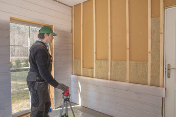 The worker makes finishing works of walls with a white wooden board, using laser line level.