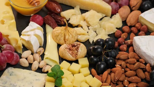 Cheese plate with camembert brie parmesan maasdam dutch cheese. Assortment of spanish or italian antipasti snack with cheese, nuts, bread, grapes, dates, figs. Top view flat lay background slow motion