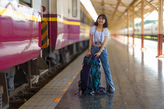 Young Asian woman traveler with a backpack on the railway, Backpack at the train station with a traveler, Travel concept. Woman traveler tourist standing at a train station.
