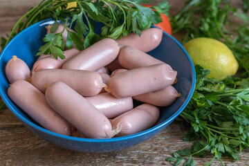 Sausages in blue bowl on the background of fresh vegetables.
