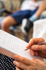 Close up of a person writing on a notebook. Adult person sitting on a sofa writing a text with an...