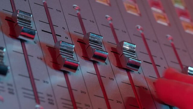Recording studio mixing desk sliders being adjusted from a an angle. Showing a hand fingers moving the sliders.