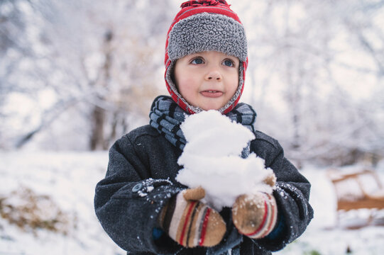 little boy holds snow in his hands and plays snowballs, close-up portrait. Snow and mittens in frosty winter forest